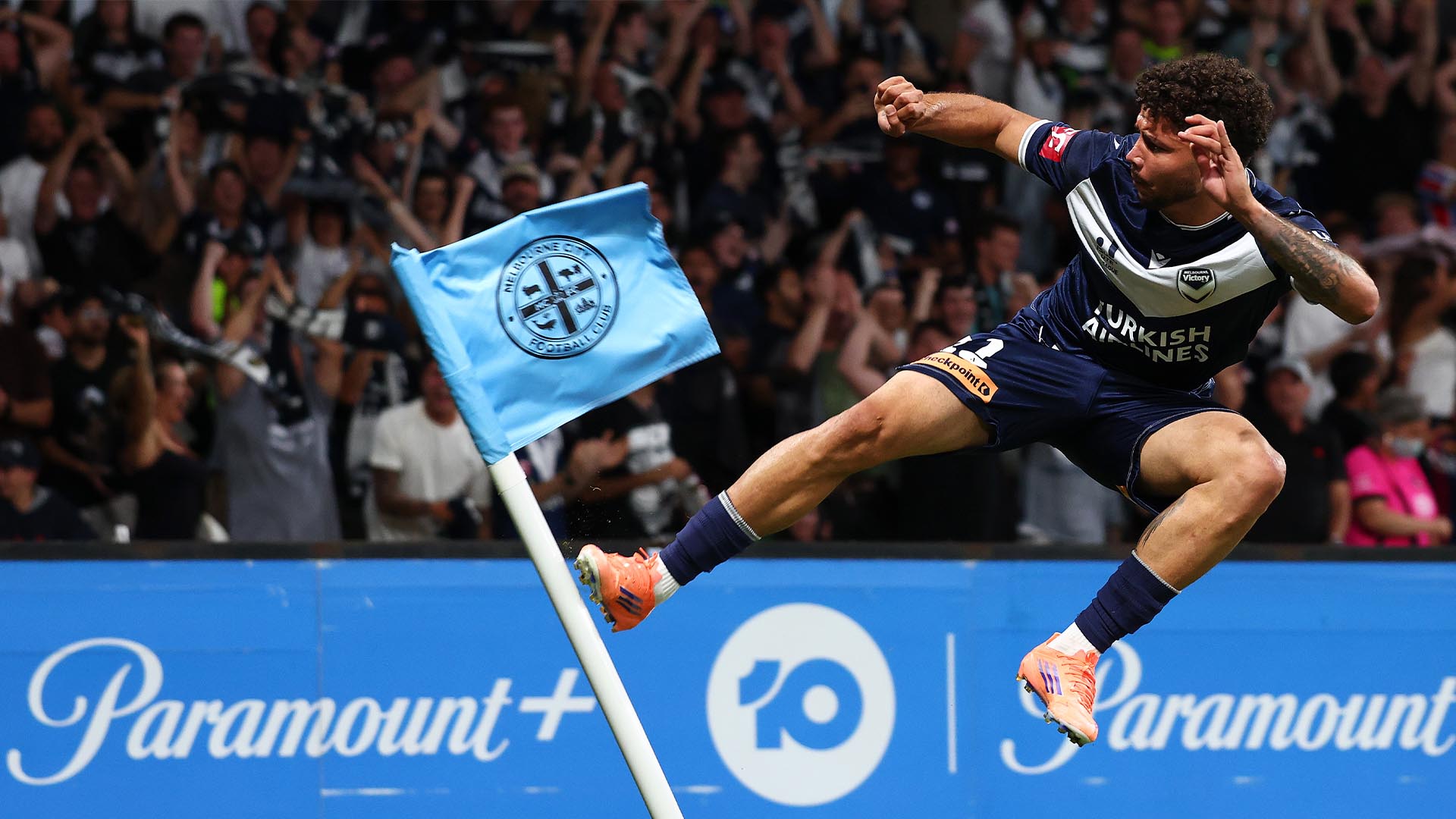 Melbourne Victory footballer jumping and kicking a Melbourne City FC themed corner flag.