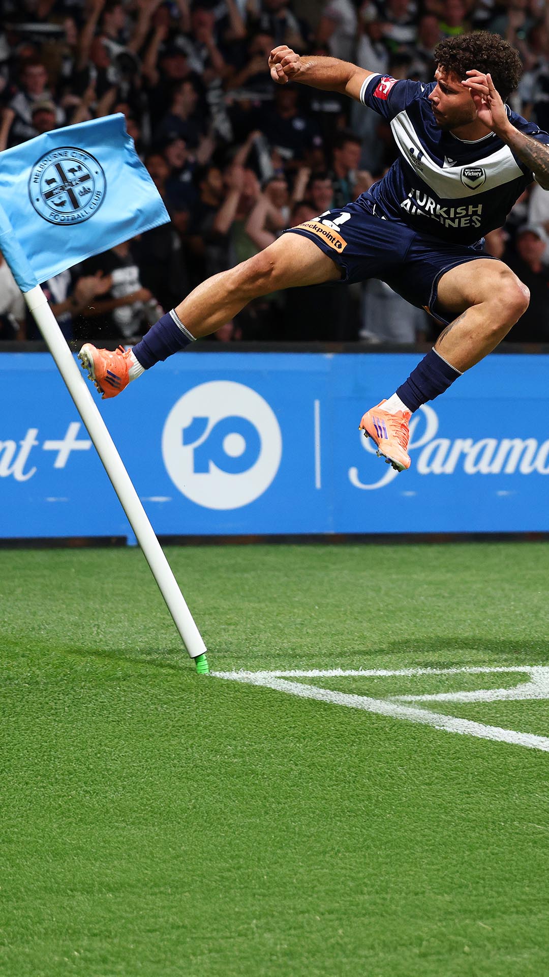 Melbourne Victory footballer jumping and kicking a Melbourne City FC themed corner flag.